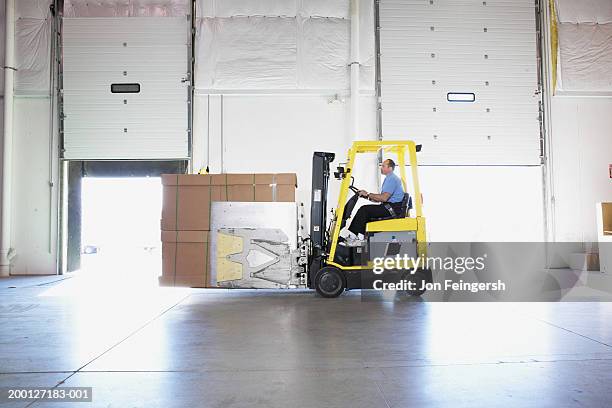 Man Driving Squeeze With Boxes Through Warehouse Side View, Bildbanksbilder