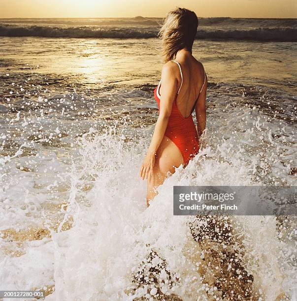 woman standing in surf, waves breaking against legs, sunset, rear view - stoneplus1 stock pictures, royalty-free photos & images