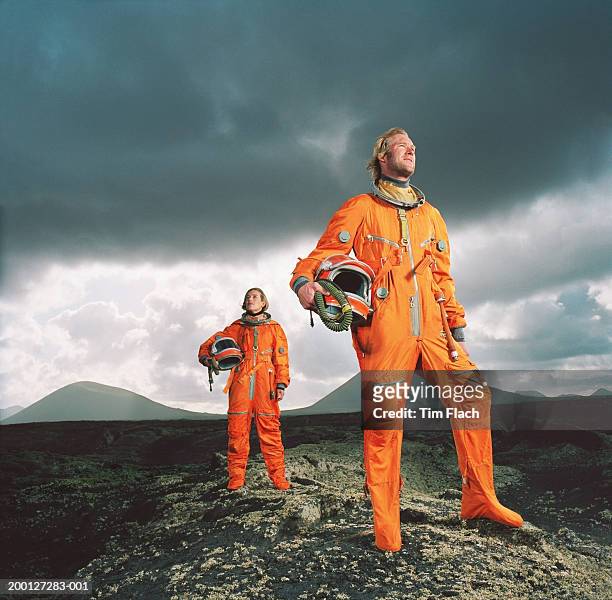 couple wearing space suits standing on rugged landscape, low angle - tim flach stock-fotos und bilder