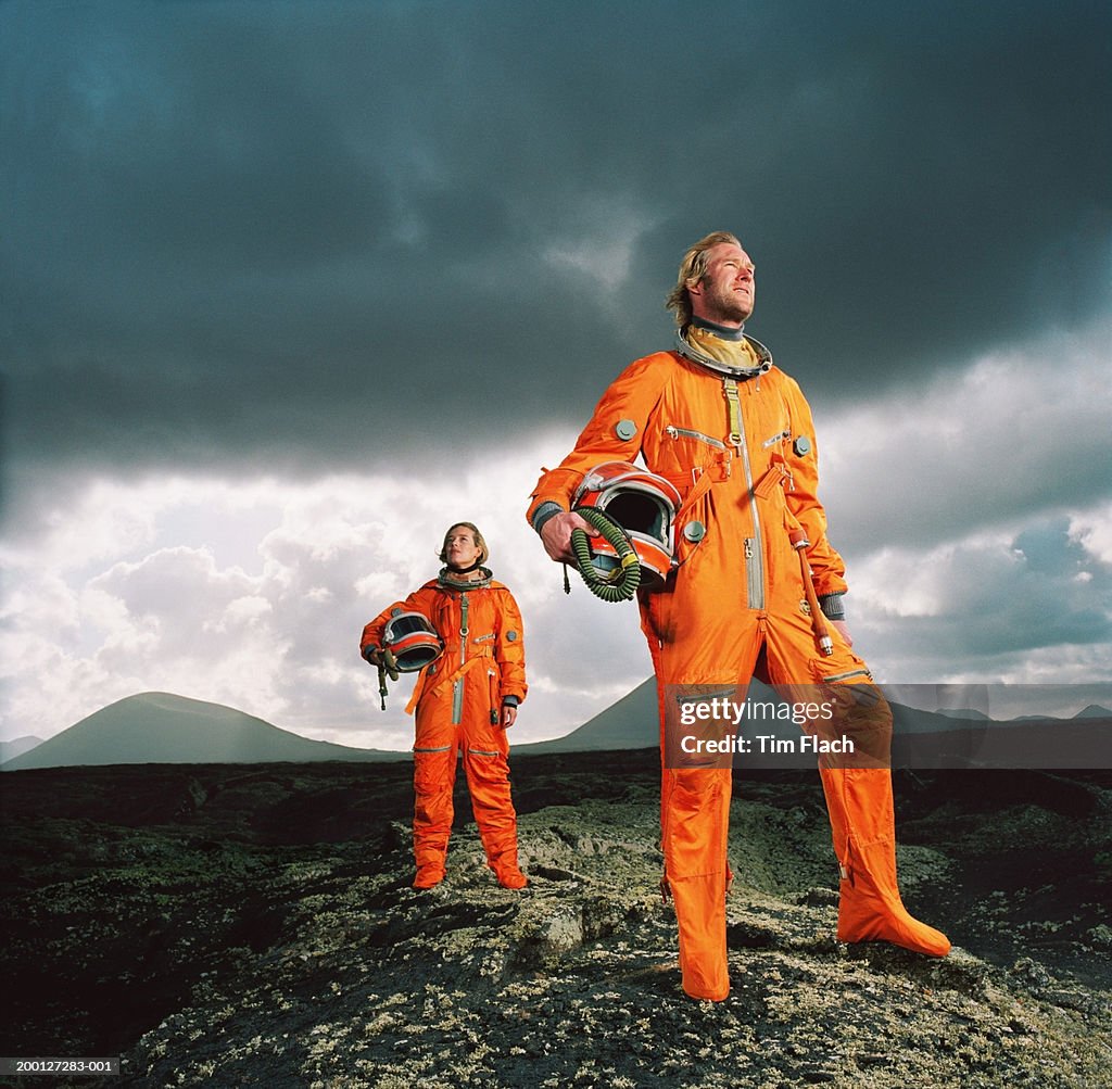 Couple wearing space suits standing on rugged landscape, low angle