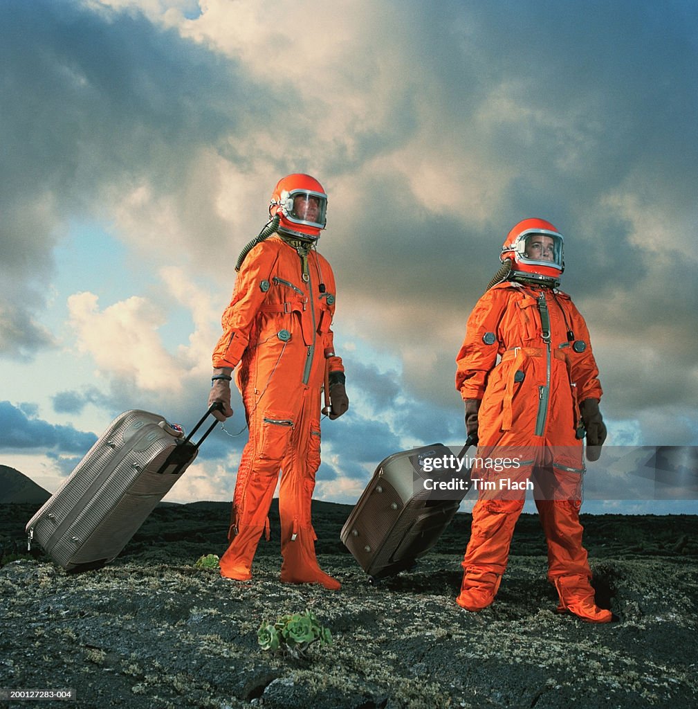 Couple wearing space suits pulling luggage across rugged landscape