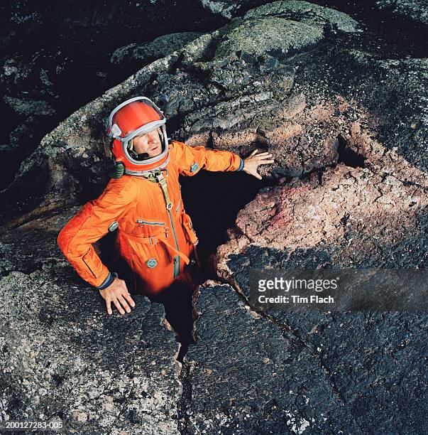 man wearing space suit climbing out of hole in rugged landscape - tim flach stock-fotos und bilder