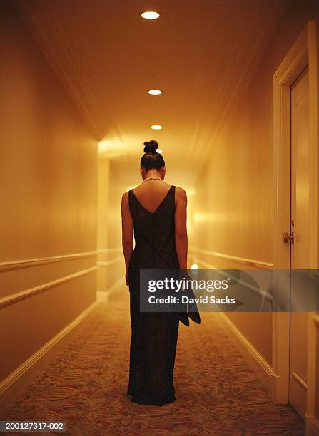 woman in formal wear holding shoes in hallway, rear view - schwarzes kleid stock-fotos und bilder