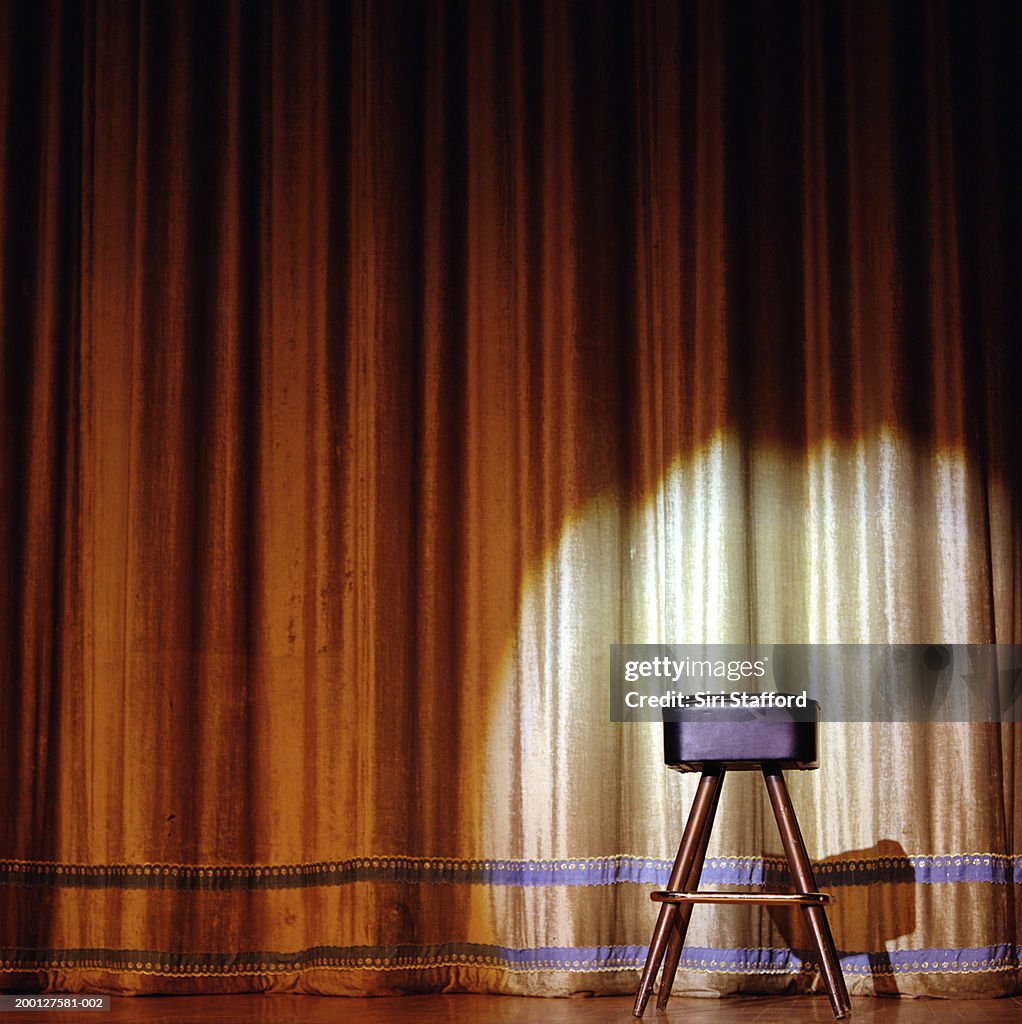 Stool sitting on stage in front of gold curtain