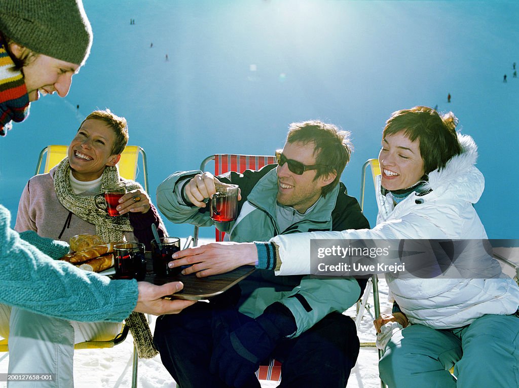 Man holding tray of bread and drinks for three friends, outdoors