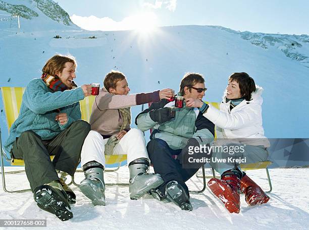 four friends in ski wear raising toast with glass mugs, outdoors - botas de après ski fotografías e imágenes de stock