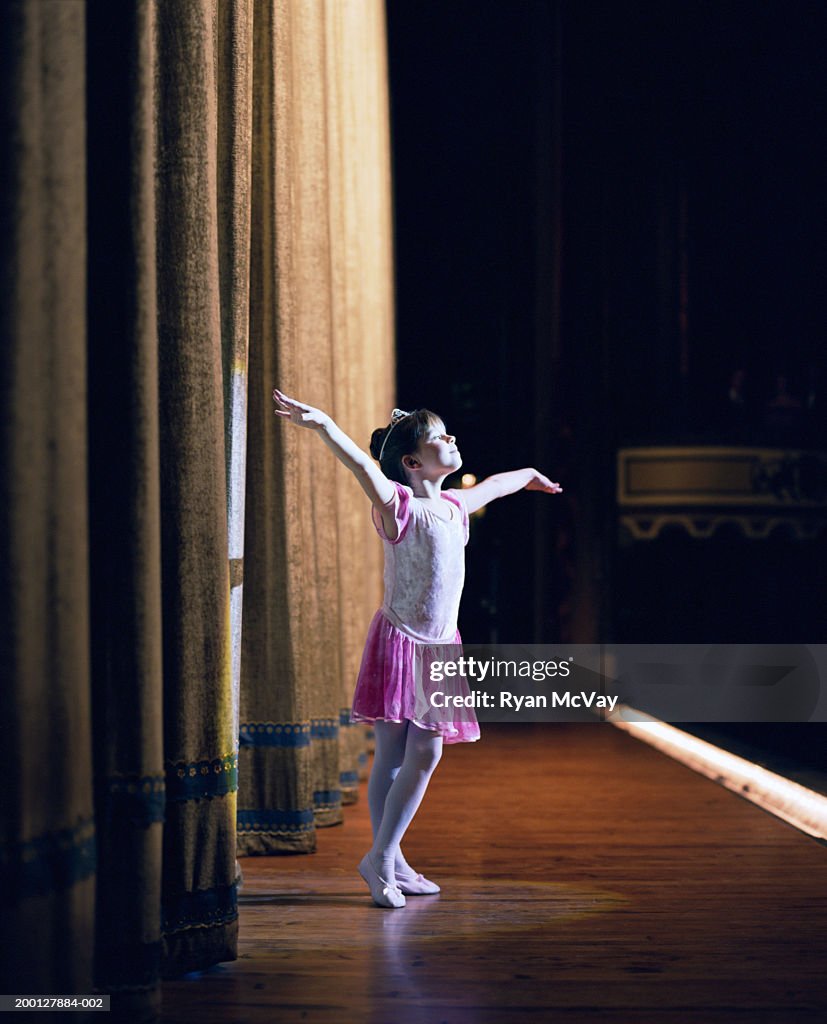 Young ballerina (6-8) standing on stage with arms outstretched