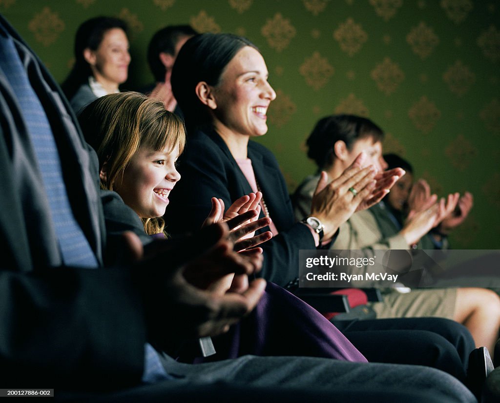 Girl (6-8) sitting between parents, applauding at theater