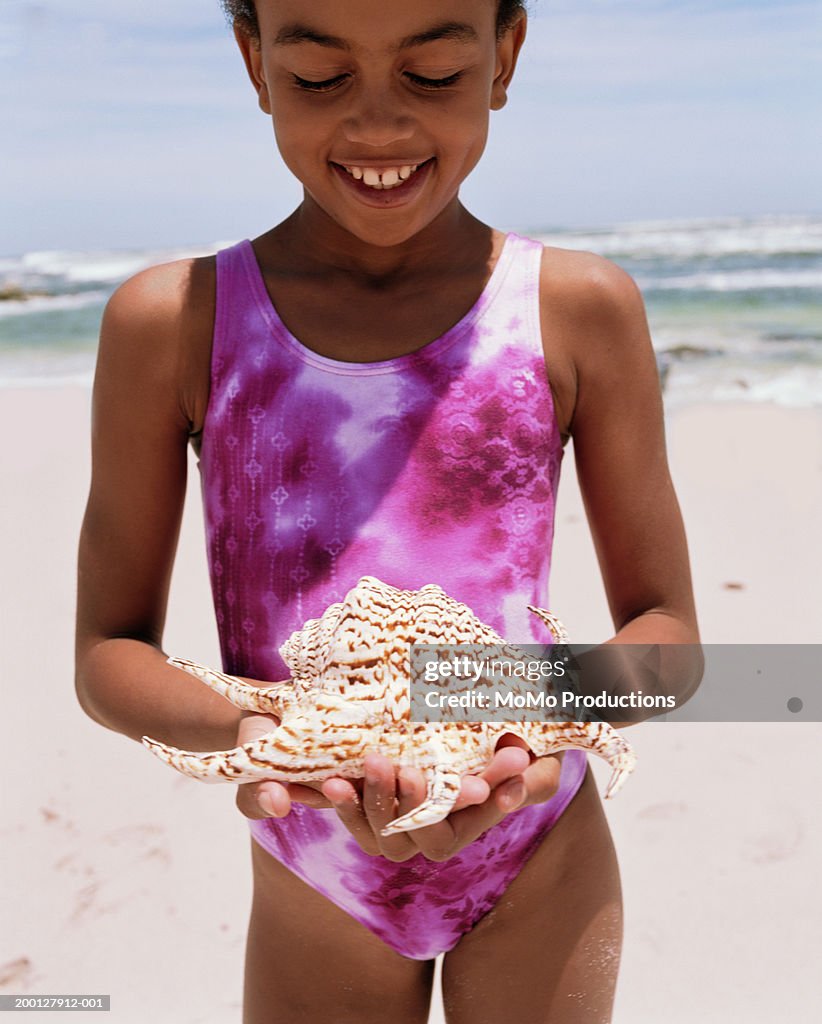 Girl (9-11) holding sea shell at beach