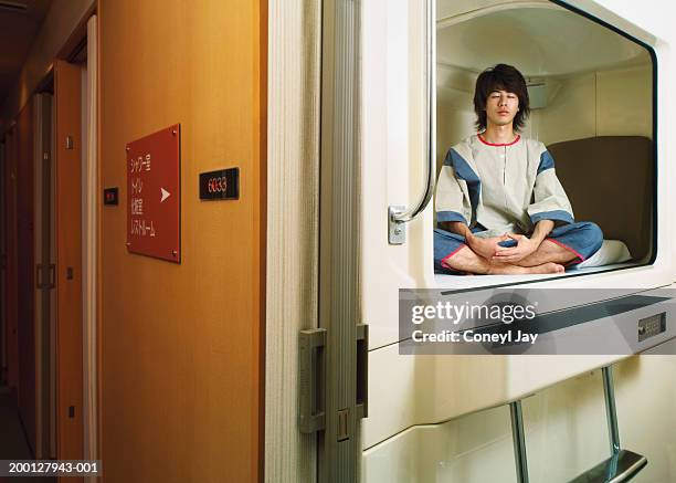 young man meditating in capsule hotel (digital composite) - travel2 stock pictures, royalty-free photos & images