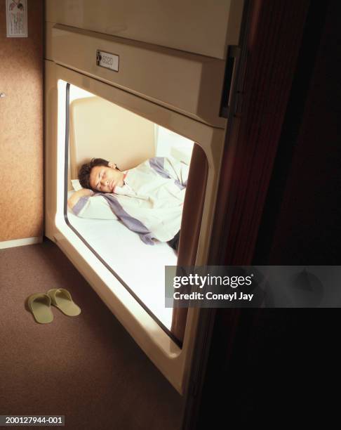 young man sleeping in capsule hotel, view through opening - capsule hotel stock pictures, royalty-free photos & images