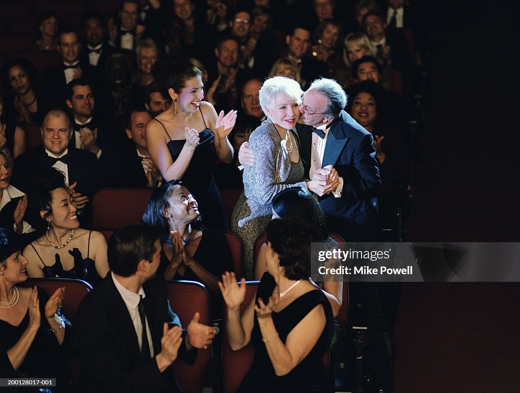 Audience applauding mature woman, husband kissing cheek