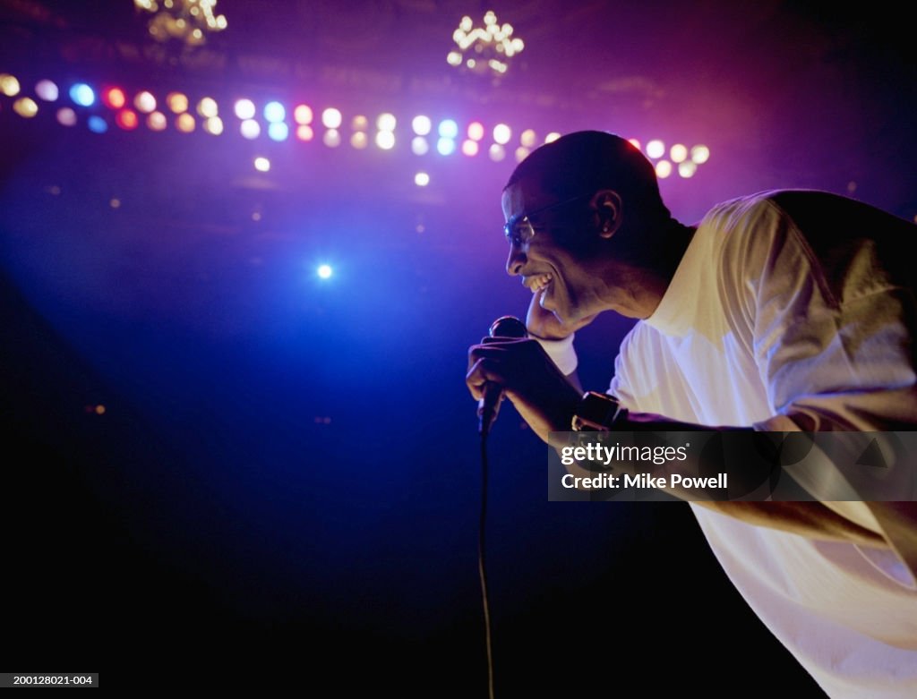 Comedian standing on stage, holding microphone, profile