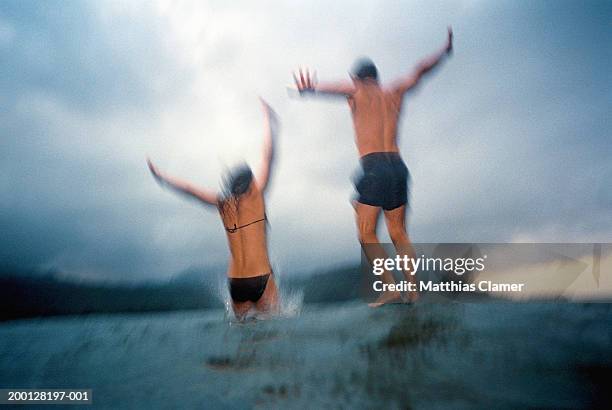 man and woman jumping into ocean, rear view (blurred motion, grainy) - den sprung wagen stock-fotos und bilder
