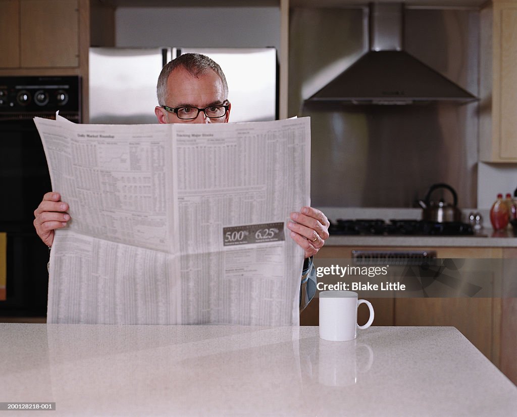 Mature man reading financial section of newspaper in kitchen