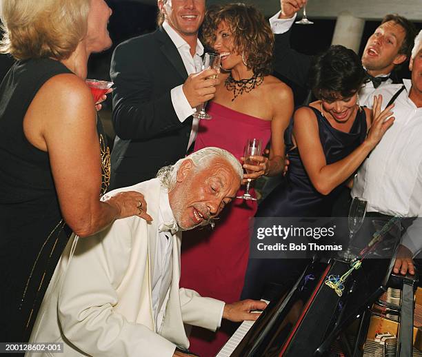 mature man playing piano surrounded by party guests - wedding guests stockfoto's en -beelden