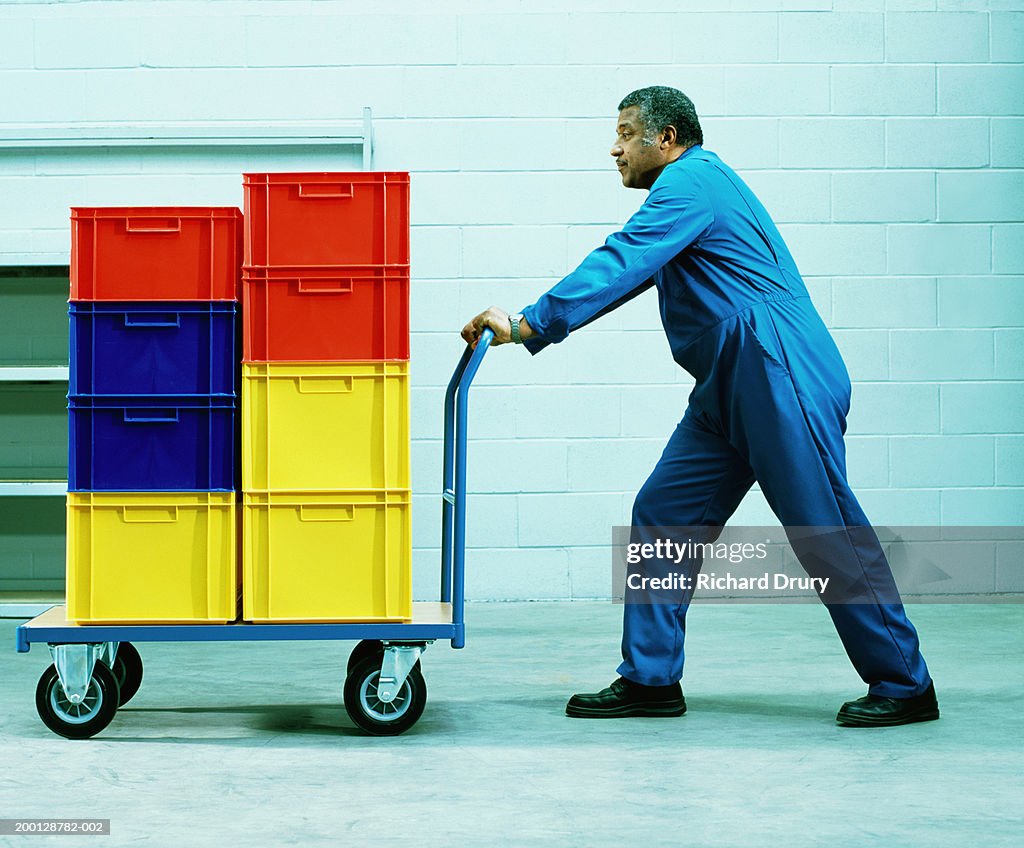 Man pushing trolley of coloured plastic boxes, side view