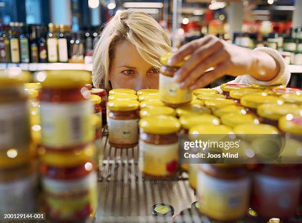 young woman selecting jar from shelf in shop (focus on woman's face) - supermercado fotografías e imágenes de stock