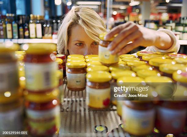 young woman selecting jar from shelf in shop (focus on woman's face) - use by label ストックフォトと画像