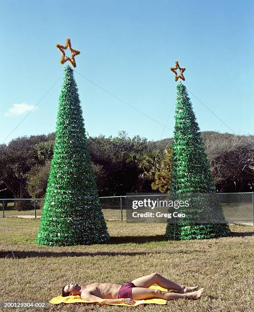 man sunbathing in front of christmas trees, side view - stoneplus1 stock pictures, royalty-free photos & images