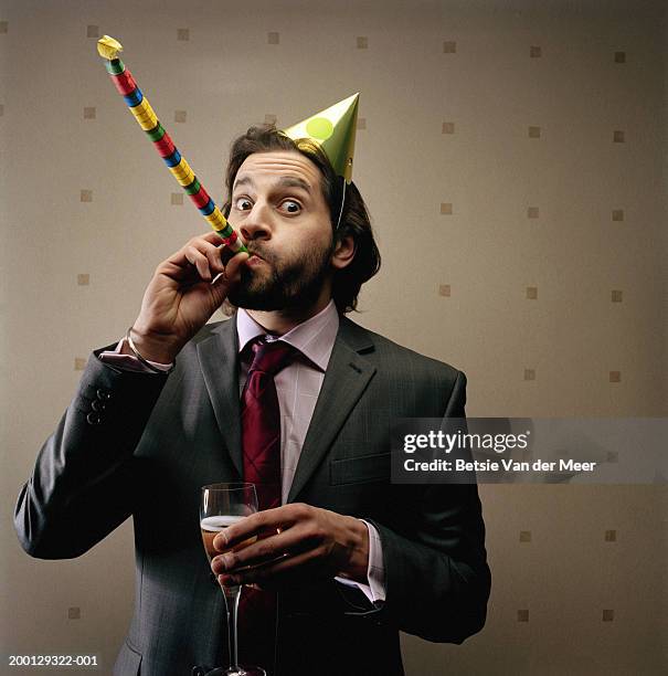 businessman wearing party hat, blowing party blower, portrait - partyhut stock-fotos und bilder