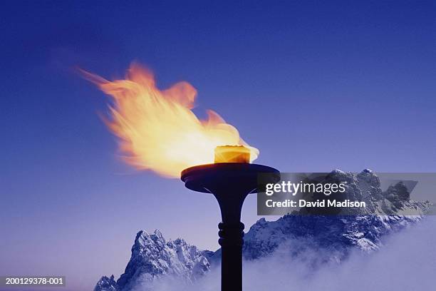 snow-covered mountains behind flaming torch (digital composite) - flaming torch stock pictures, royalty-free photos & images