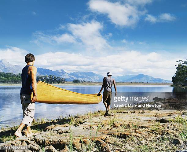 south africa, cape province, two young men carrying canoe by lake - travel2 stock pictures, royalty-free photos & images
