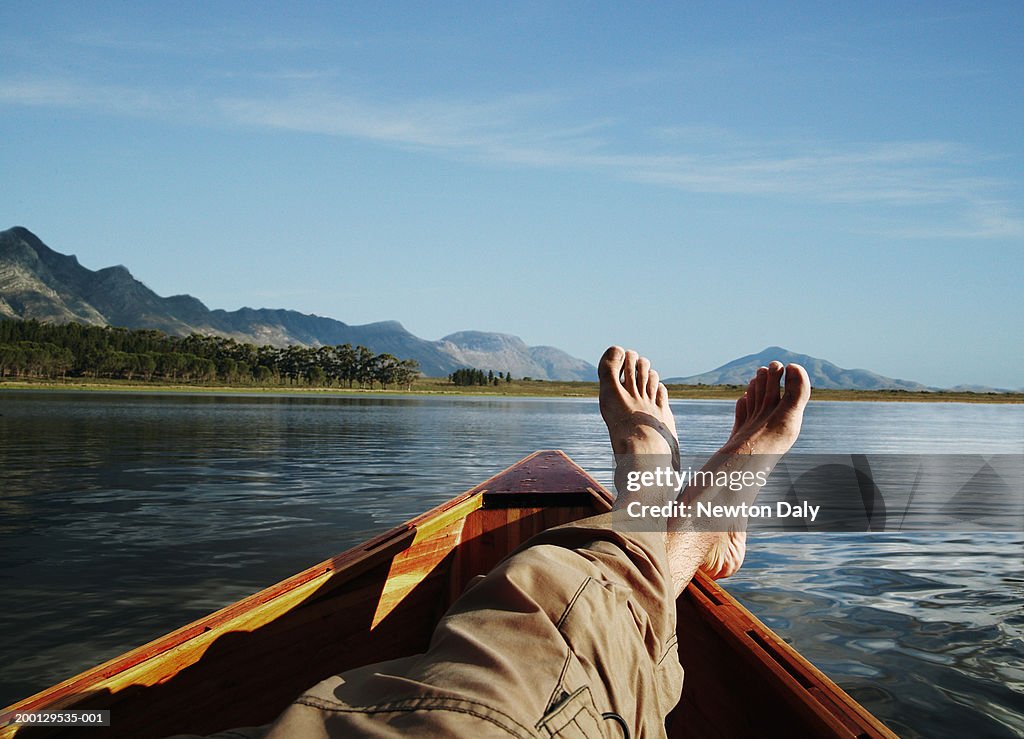Young man lying in boat on lake, low section