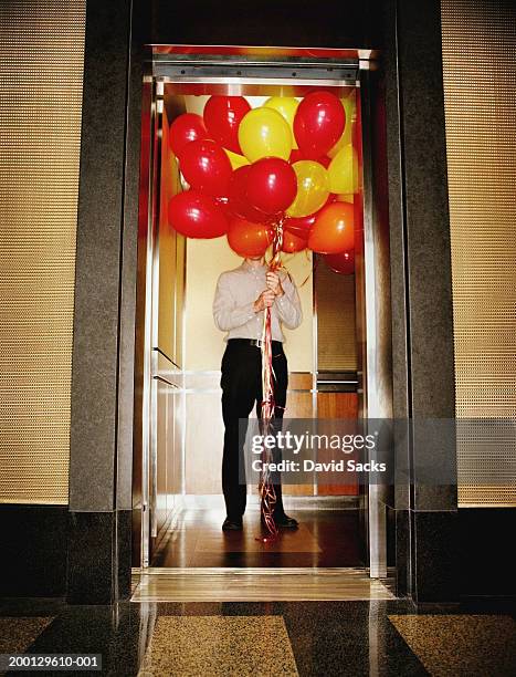 man in elevator holding large bundle of balloons - aufzug business stock-fotos und bilder