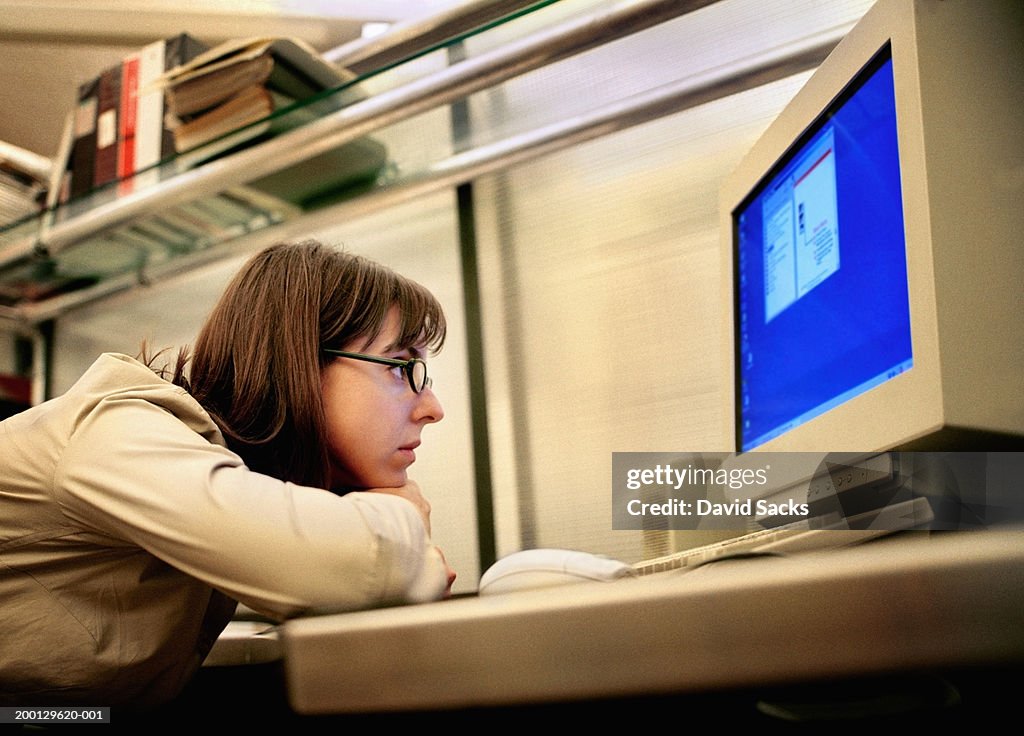 Woman resting head on arms, looking at computer monitor in office