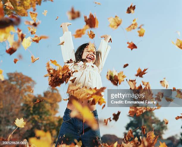 girl (8-10) tossing leaves in air, autumn, low angle view - automne feuilles photos et images de collection