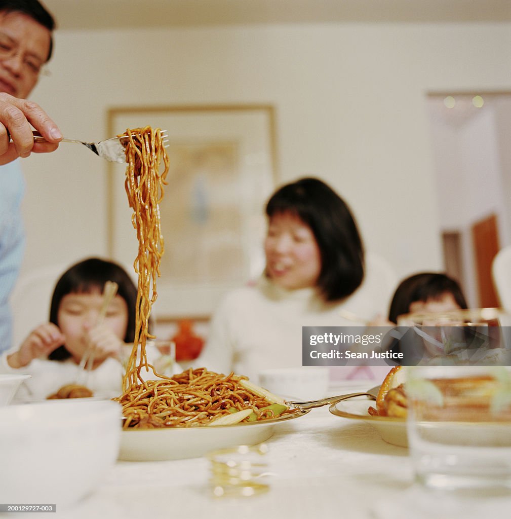 Mature man serving noodles at dinner table (focus on noodles)