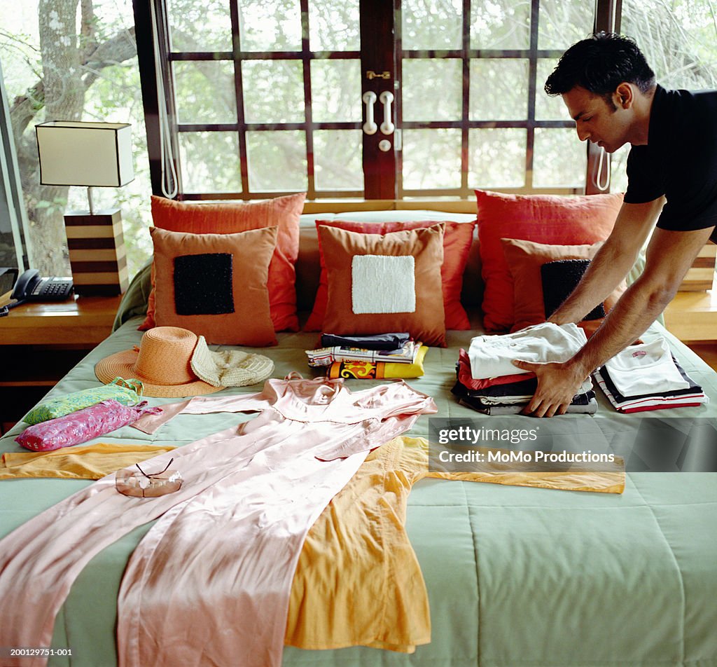 Young man laying clothes out on bed at safari lodge, side view