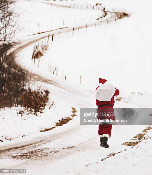 man in santa suit with sack over shoulder on snowy lane, rear view - claus lange stock pictures, royalty-free photos & images