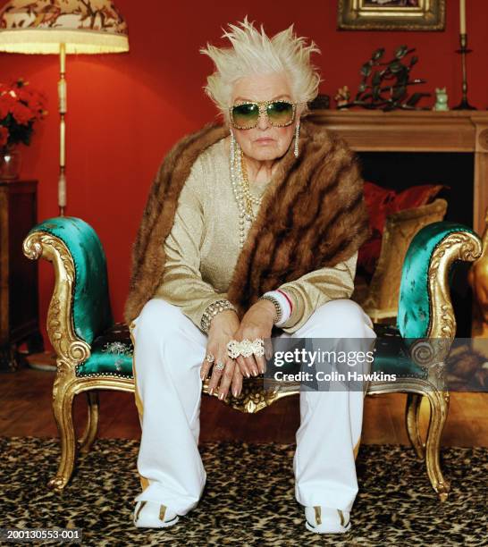 senior woman on chaise longue, wearing hip hop accessories, portrait - jong van hart stockfoto's en -beelden