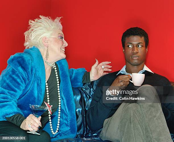 senior woman gesturing to young man relaxing on sofa - generation gap stock pictures, royalty-free photos & images