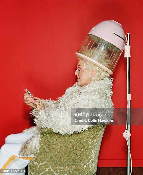 senior woman sitting under hairdryer using mobile phone, side view - hair dryer - fotografias e filmes do acervo