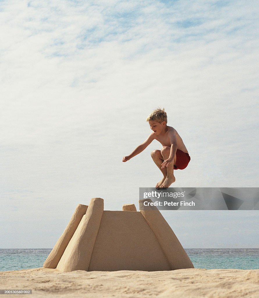 Boy (9-11) jumping onto large sandcastle