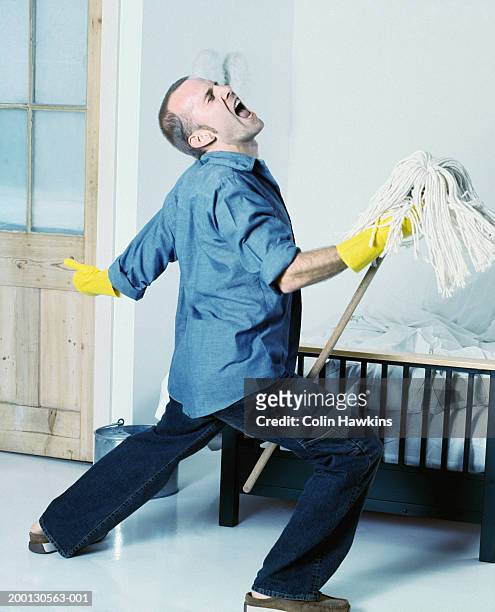 man wearing rubber gloves singing, using mop as 'microphone stand' - aljofifa fotografías e imágenes de stock
