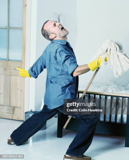 man wearing rubber gloves singing, using mop as 'microphone stand' - man singing stockfoto's en -beelden