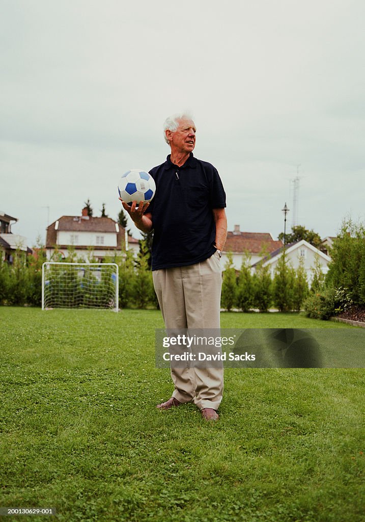 Senior man holding soccer ball on field