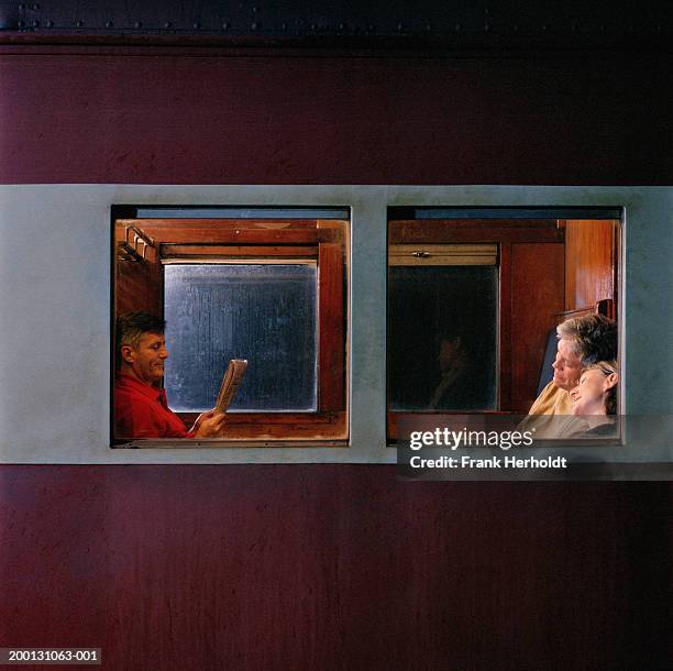 mature couple and man with newspaper on train, view through window - treincoupé stockfoto's en -beelden
