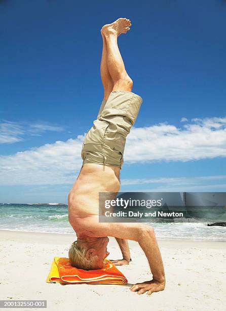 senior man performing headstand on beach, side view - senior yoga stock-fotos und bilder