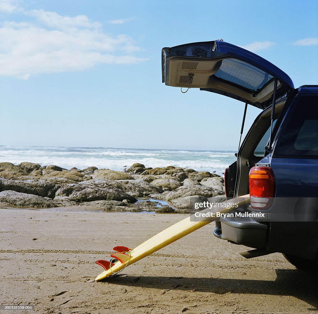 Surfboard leaning against open boot of SUV on beach