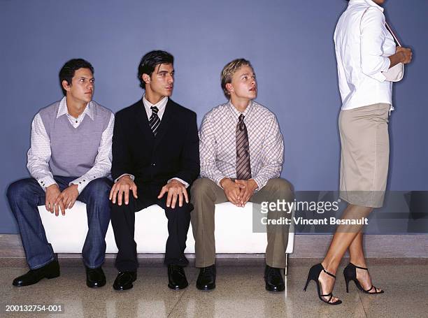 three young men on bench indoors watching woman walking past - female with group of males stock pictures, royalty-free photos & images
