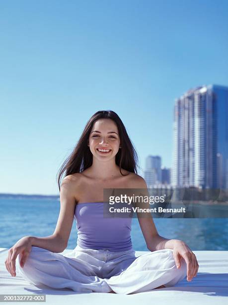 teenage girl (15-17) sitting cross legged by sea, portrait - purple pants stock-fotos und bilder