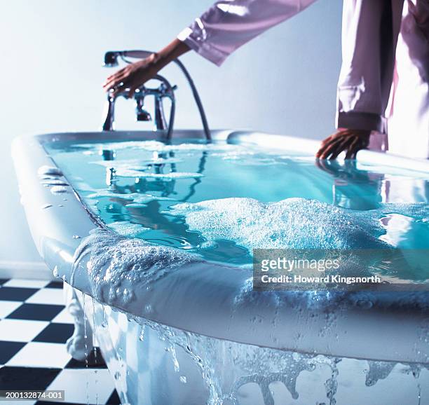 woman turning bath tap, water overflowing (focus on edge of bath) - waters edge imagens e fotografias de stock