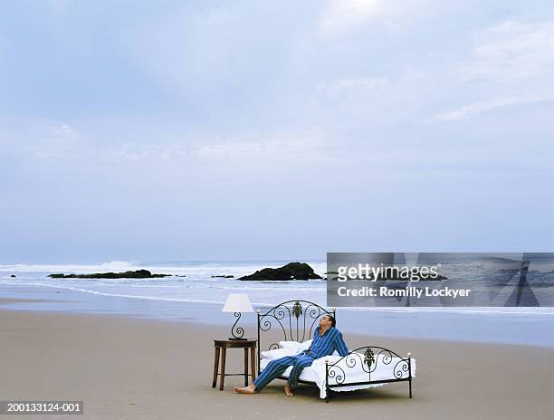 man wearing pyjamas sitting on bed on beach - bedside table lamp stock pictures, royalty-free photos & images