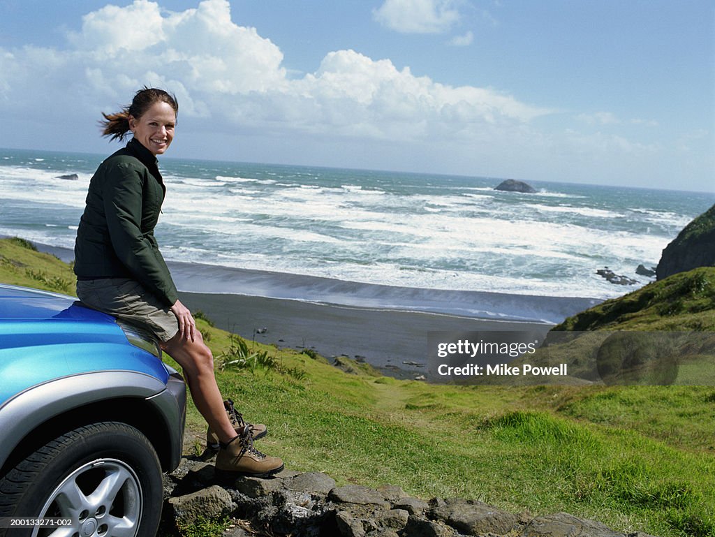 Woman sitting on hood of car, beach in background