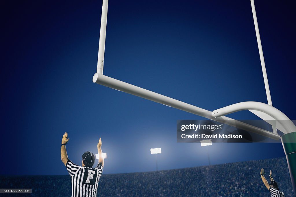 Two American football referees giving touchdown signal, rear view